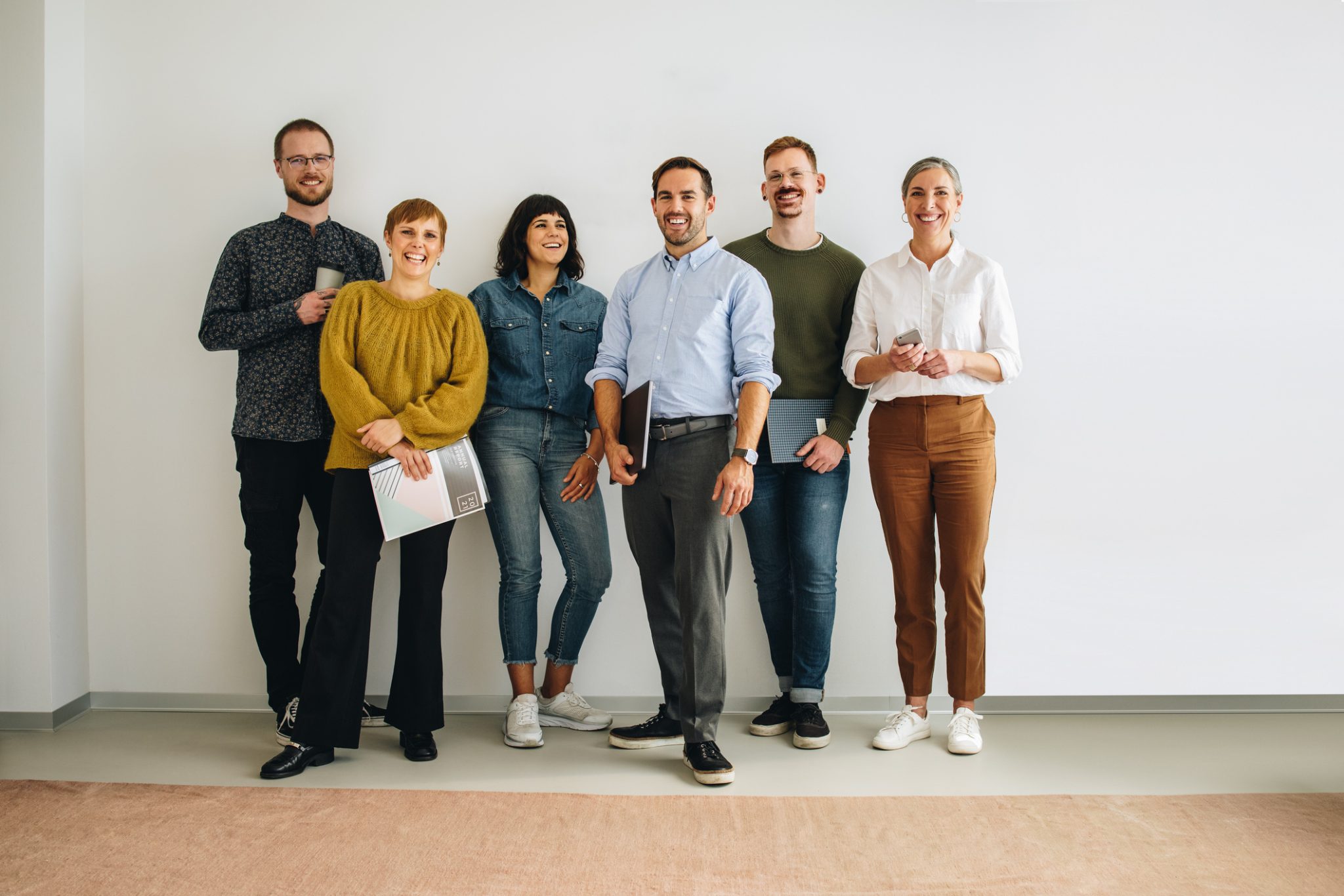 Successful creative team standing against wall looking at camera. Colleagues standing at wall in office.
