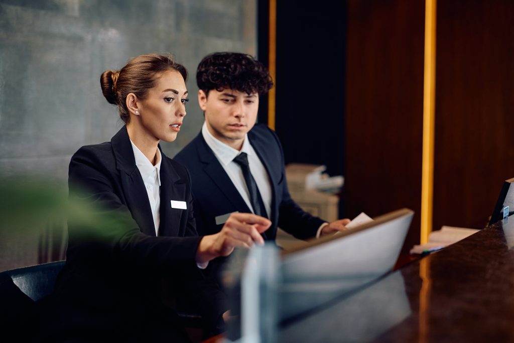 Female concierge assisting receptionist while suing desktop PC in a hotel. Copy space.