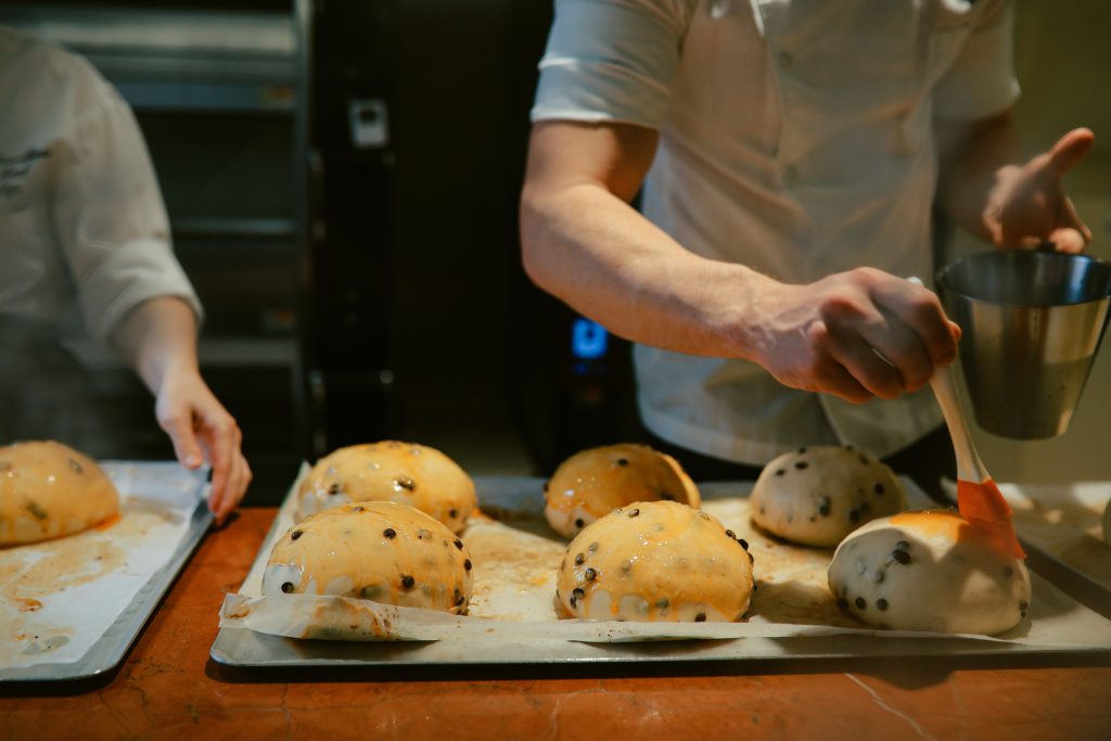 Young man, a small business owner, working in a lovely French bakery in Tokyo, Japan. He is preparing brioche buns and croissants, enjoying his work.