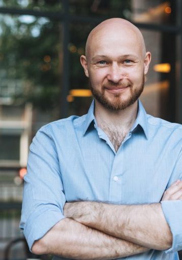 Portrait of Adult bald smiling attractive man forty years with beard in blue shirt businessman against glass wall of street cafe