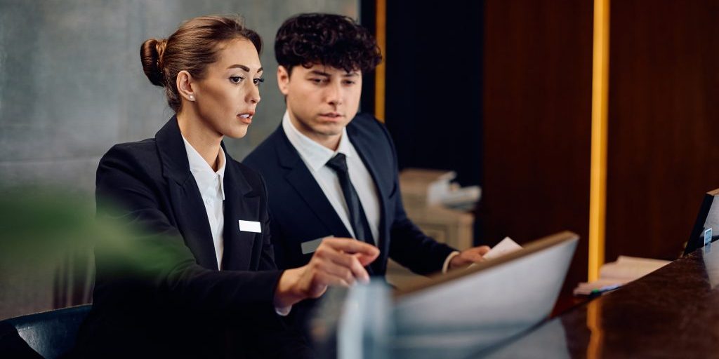 Female concierge assisting receptionist while suing desktop PC in a hotel. Copy space.